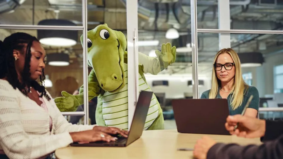 Crocs mascot Niles sitting in an office meeting