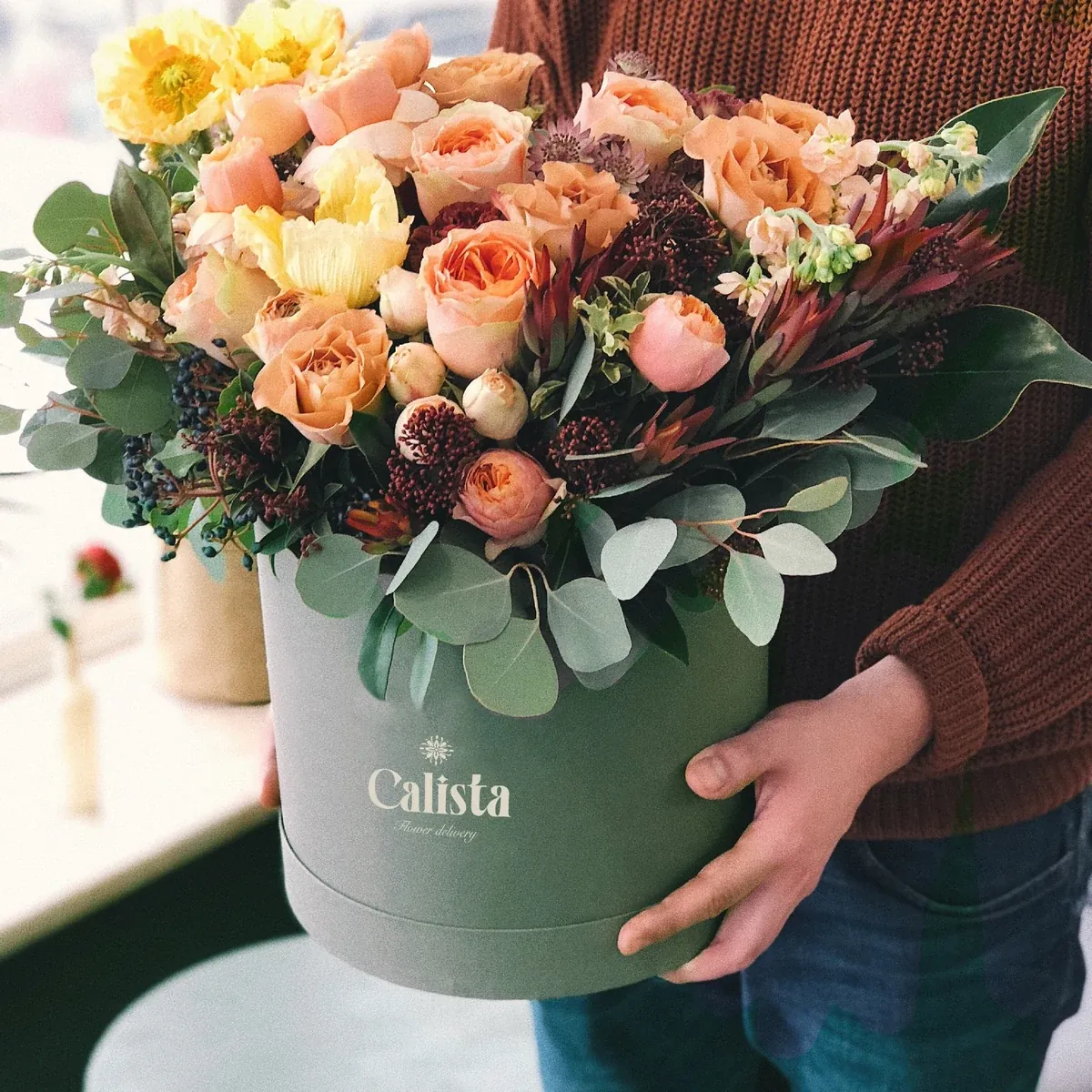 Calista: a branded hatbox of flowers carried in both arms