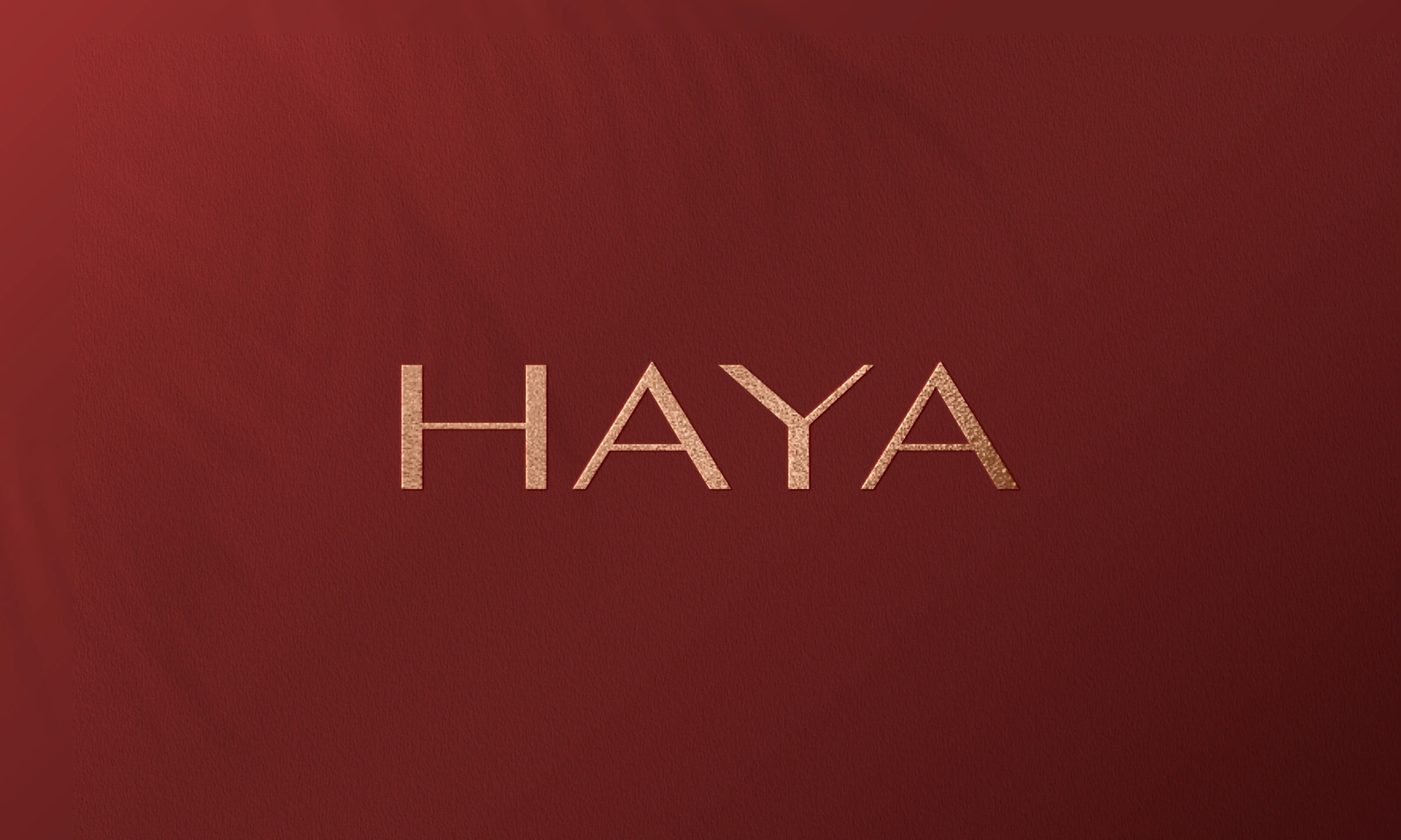 Haya: the wordmark in gold on oxblood