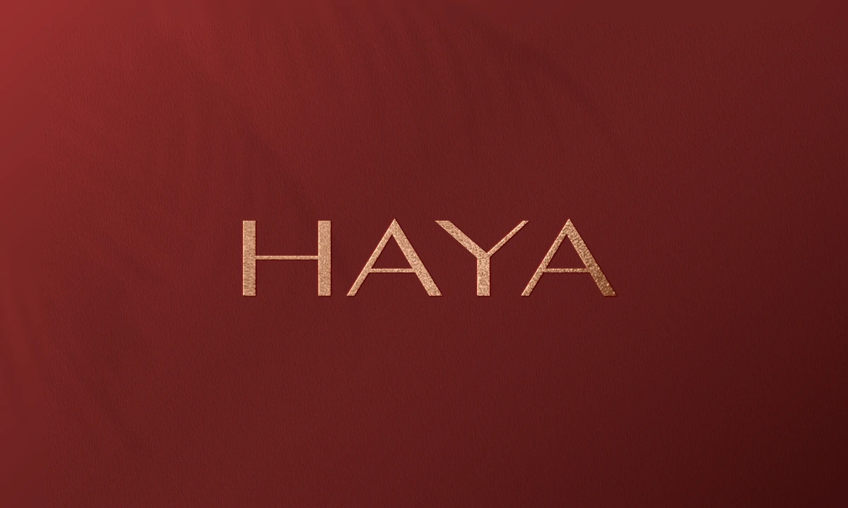 Haya: the wordmark in gold on oxblood